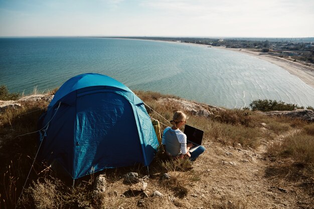 Donna felice che si siede vicino alla tenda con il computer portatile