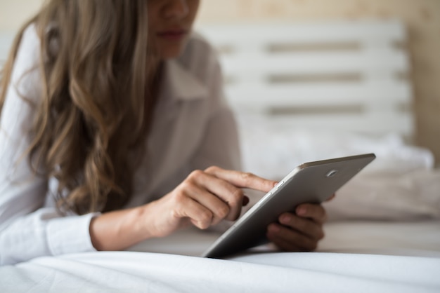 Donna felice che si trova sul letto con computer tablet