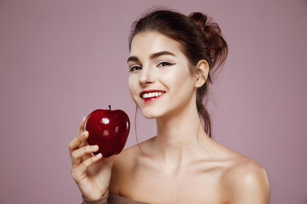 Donna felice che sorride tenendo mela rossa sul rosa