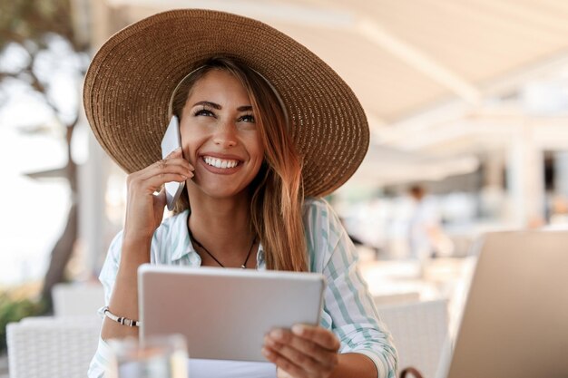 Donna felice che usa la tavoletta digitale e comunica sul cellulare mentre è seduto in un bar