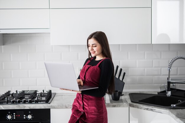 Donna felice che utilizza computer portatile a casa nella cucina