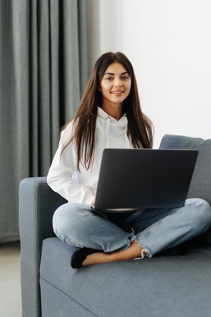 Donna felice che utilizza computer portatile seduto sul divano accogliente