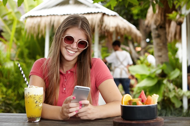 Donna felice che utilizza la connessione wi-fi gratuita sul suo telefono cellulare, guardando lo schermo con un sorriso gioioso flirtare