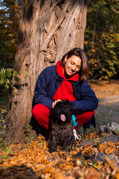 Donna felice con il cane nel parco con foglie autunnali