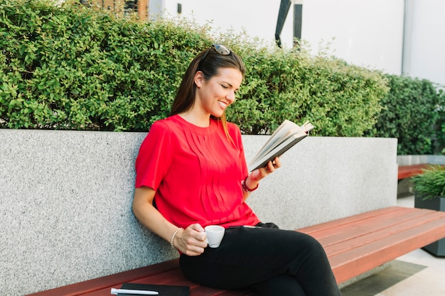 Donna felice con il libro di lettura della tazza di caffè