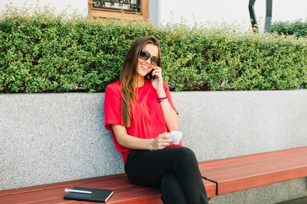 Donna felice con la tazza di caffè che parla sullo smartphone