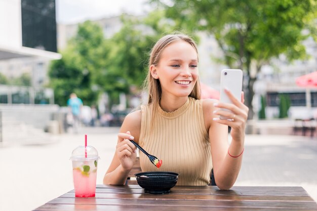 Donna felice con smartphone che prende selfie al caffè di strada