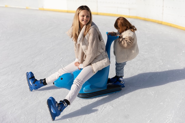 Donna felice del colpo pieno con il bambino alla pista di pattinaggio