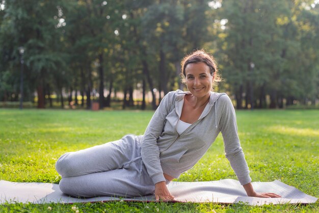 Donna felice della foto a figura intera che si siede sulla stuoia di yoga