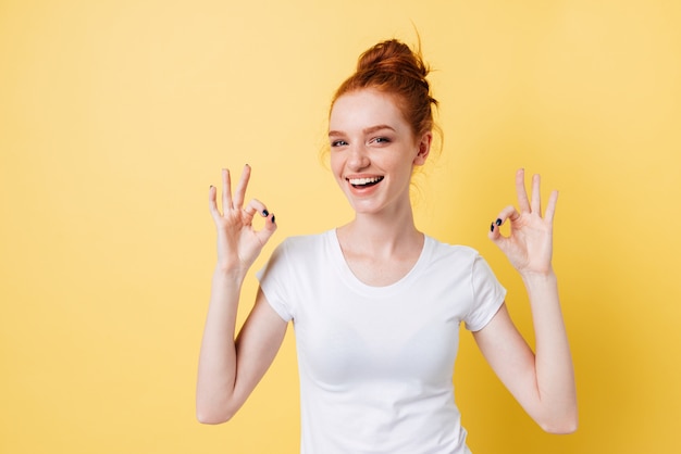 Donna felice dello zenzero che mostra i segni giusti con entrambe le mani