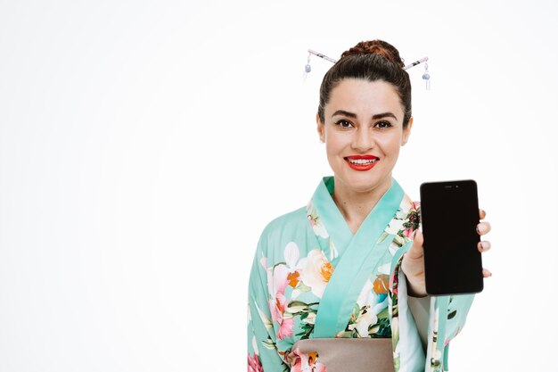 Donna felice e contenta in kimono giapponese tradizionale che mostra smartphone su white