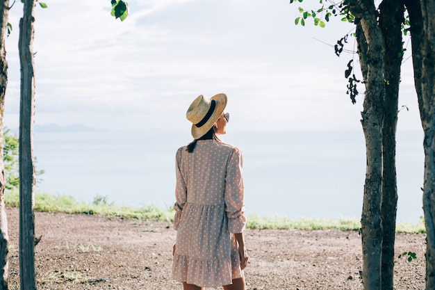 Donna felice in abito carino estivo e cappello di paglia in vacanza con viste esotiche tropicali