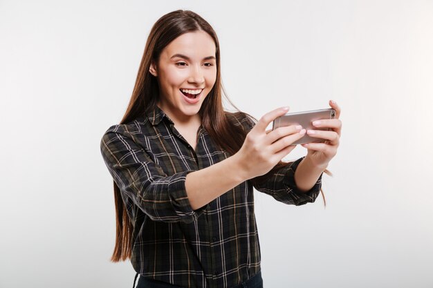 Donna felice in camicia che gioca sul telefono