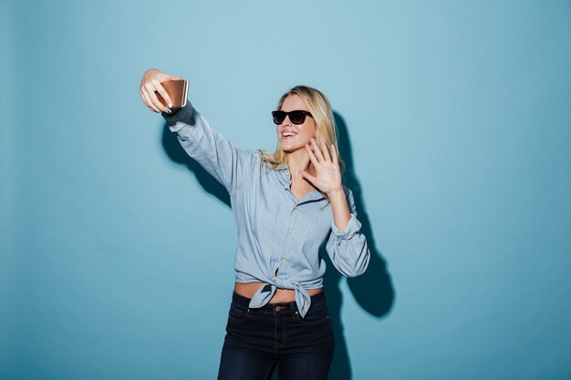 Donna felice in camicia e occhiali da sole che fanno selfie sullo smartphone
