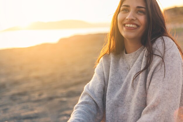 Donna felice in maglione che si siede sulla riva del mare sabbioso