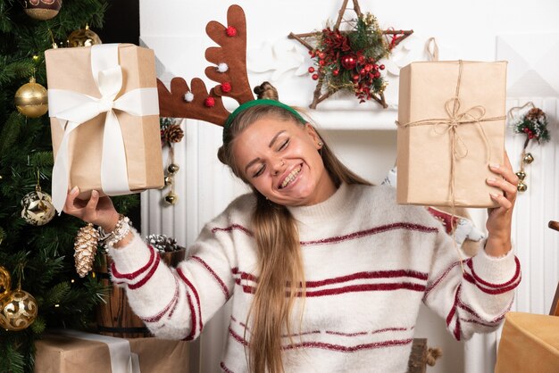 Donna felice in orecchie di cervo che tengono due regali di Natale.