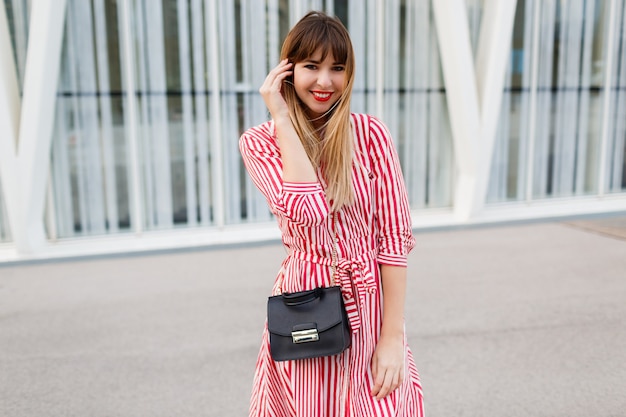 Donna felice in vestito rosso che propone sulla strada.