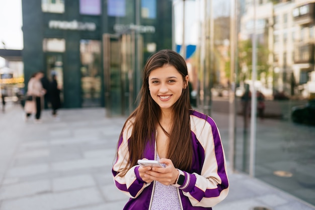 Donna felice per strada che usa uno smartphone e guarda davanti