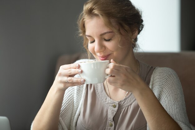 Donna felice sorridente bere caffè aromatico con gli occhi chiusi