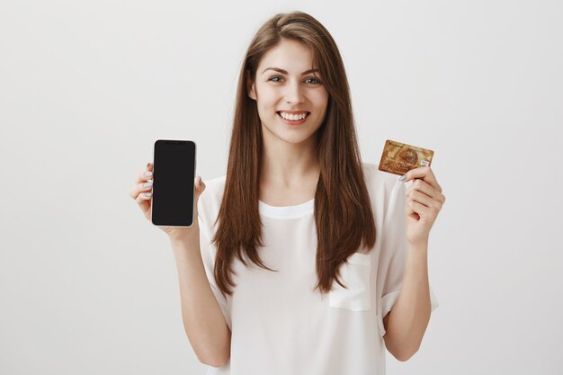 Donna felice sorridente che mostra il display del telefono cellulare e la carta di credito. Promozione dell'applicazione per lo shopping