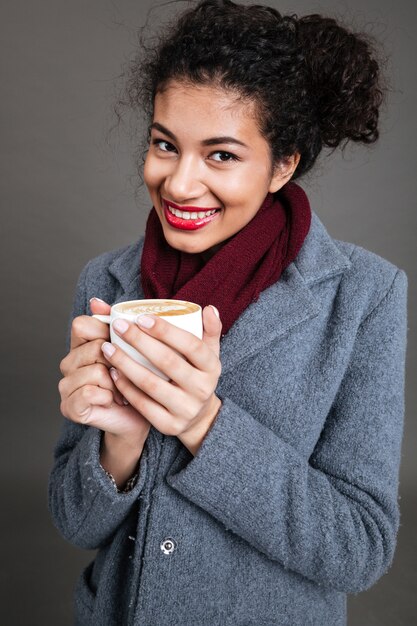 Donna felice sorridente in cappotto che tiene tazza di caffè