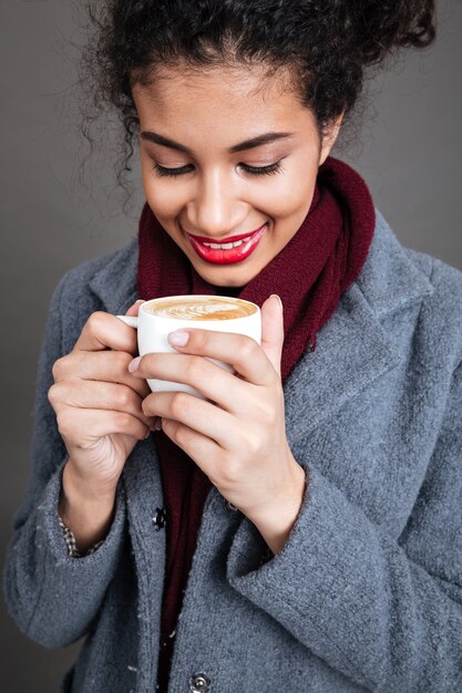 Donna felice sorridente in cappotto che tiene tazza di caffè