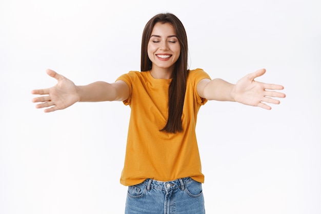 Donna femminile allegra e romantica raggiunge le mani verso la telecamera, allarga le braccia lateralmente per coccolare o abbracciare qualcuno, chiudi gli occhi aspettando che ti avvicini, sorridendo soddisfatto e felice, sfondo bianco