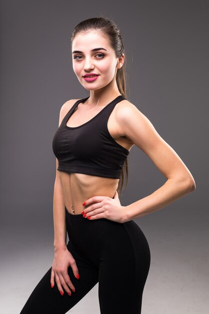 Donna femminile di forma fisica con l'ente muscolare pronto per l'allenamento sulla parete grigia