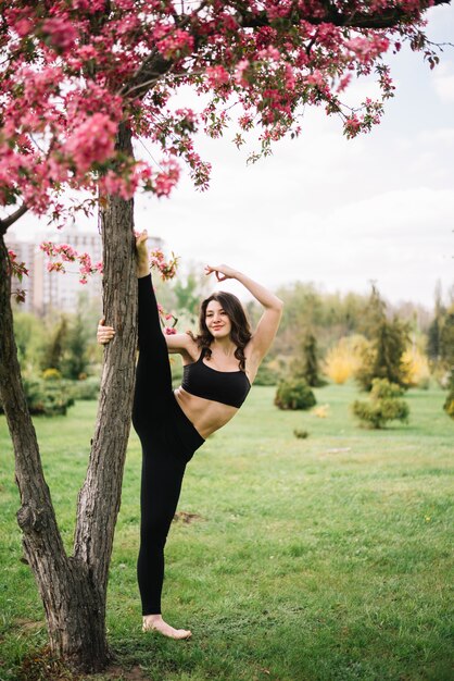 Donna flessibile che si esercita vicino all'albero in parco