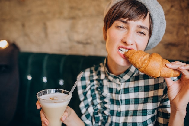 Donna francese in caffè bevendo latte e mangiando croissant