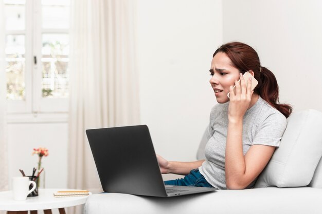 Donna frustrata che parla sul telefono mentre esaminando computer portatile