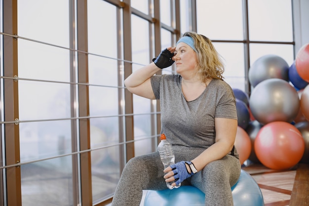 Donna grassa a dieta, fitness. Signora seduta su un fitball e beve acqua.