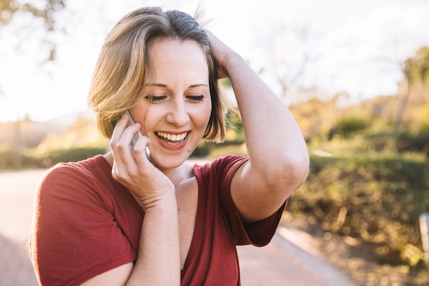 Donna graziosa che comunica sul telefono sul vicolo del parco