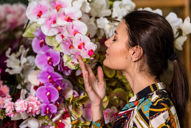 Donna graziosa che odora i fiori rosa in serra