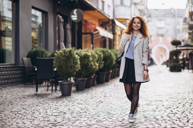 Donna graziosa con capelli ricci che cammina in una strada del caffè