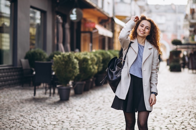 Donna graziosa con capelli ricci che cammina in una strada del caffè