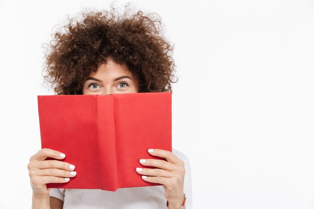 Donna graziosa con capelli ricci che dà una occhiata da un libro