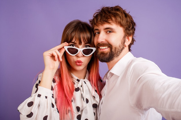 Donna graziosa con il sorriso schietto e capelli rosa che posano con il suo ragazzo con la barba