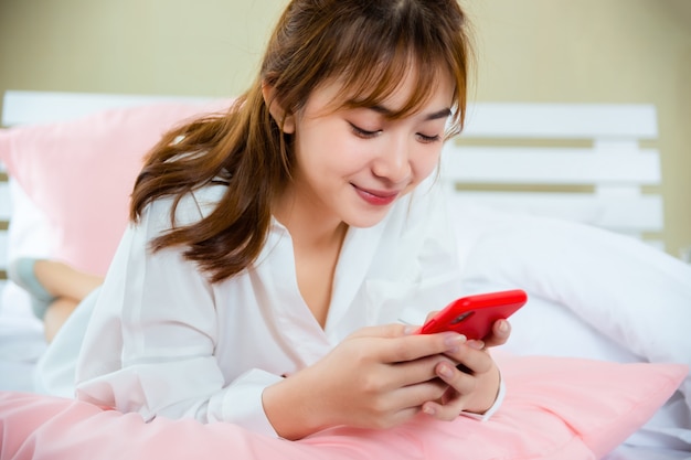 Donna graziosa felice che per mezzo dello smartphone sul letto