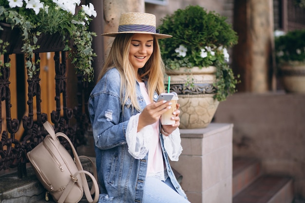 Donna graziosa in cappello che comunica sul telefono e che beve caffè