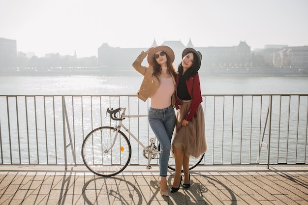 Donna graziosa in jeans in posa con la sorella bruna all'argine