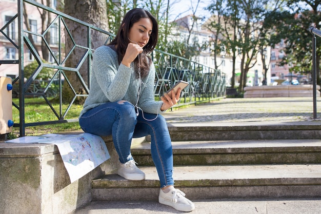 Donna graziosa seria che ascolta la musica sul parapetto delle scale della città