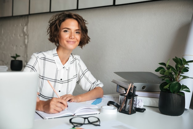 Donna graziosa sorridente che lavora dalla tabella