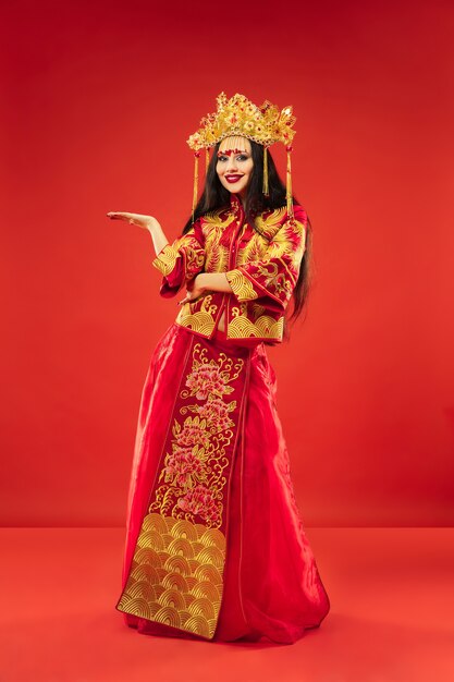 Donna graziosa tradizionale cinese allo studio sopra la parete rossa