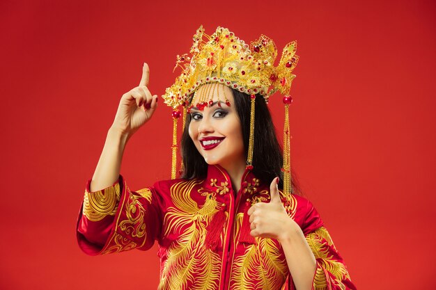 Donna graziosa tradizionale cinese in studio su sfondo rosso. Bella ragazza che indossa il costume nazionale. Capodanno cinese, eleganza, grazia, performer, performance, danza, attrice, concetto di abbigliamento