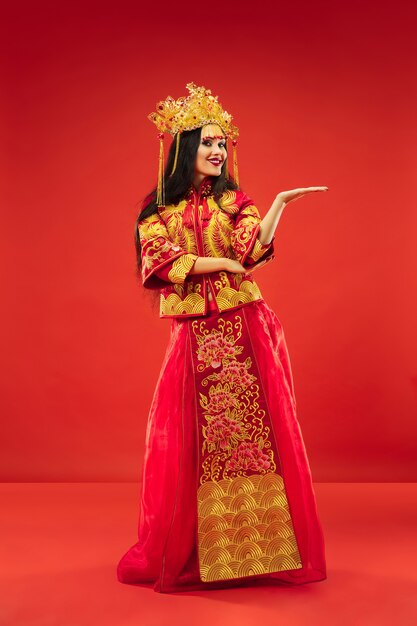 Donna graziosa tradizionale cinese in studio su sfondo rosso. Bella ragazza che indossa il costume nazionale. Capodanno cinese, eleganza, grazia, performer, performance, danza, attrice, concetto di abbigliamento