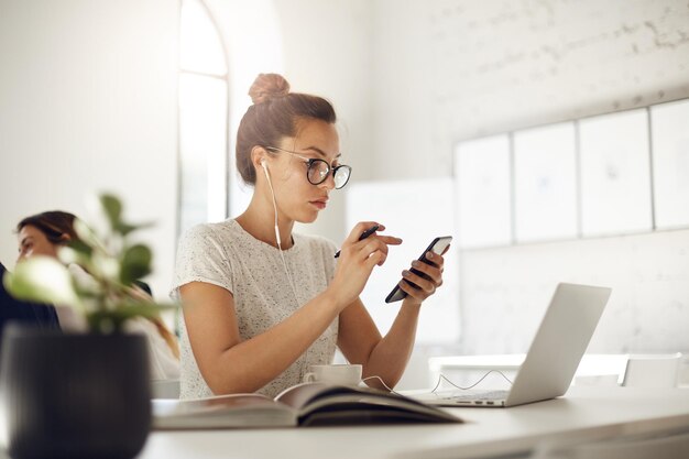 Donna impegnata che utilizza smartphone e laptop con una conversazione di lavoro online in un bar o una piattaforma di coworking che beve caffè Concetto di business