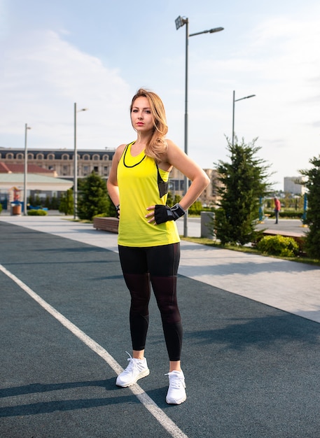 Donna in abiti sportivi gialli e neri in piedi e in posa su una linea da jogging.