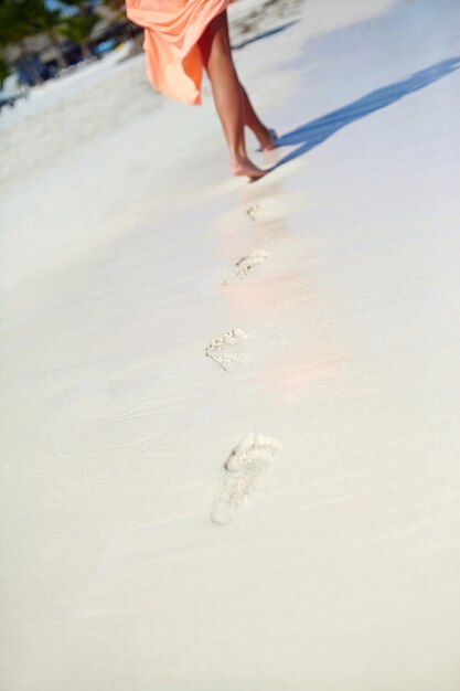donna in abito colorato che cammina sulla spiaggia dell'oceano lasciando impronte nella sabbia