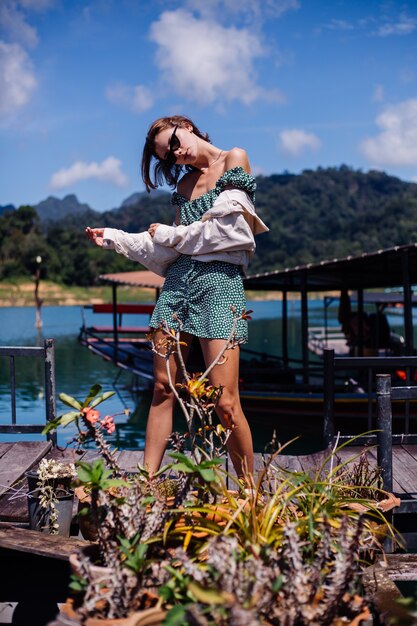 Donna in abito estivo e giacca turistica viaggia in Thailandia, parco nazionale di Khao Sok, splendida vista sulle barche e sul lago.